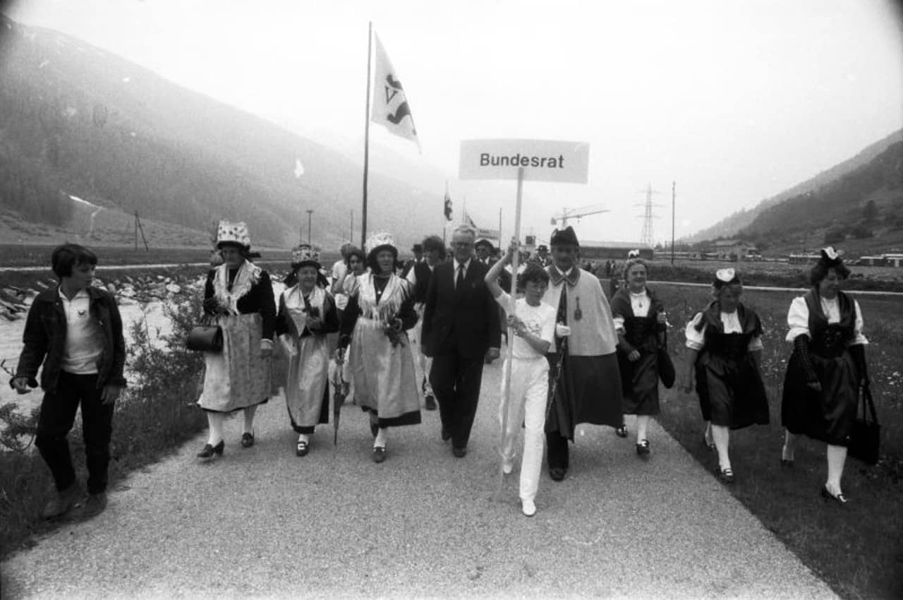 Der Bundesrat Leon Schlumpf wird an der Eröffnung des Furka-Eisenbahn-Tunnels von Frauen in Tracht und einem Jungen begleitet.