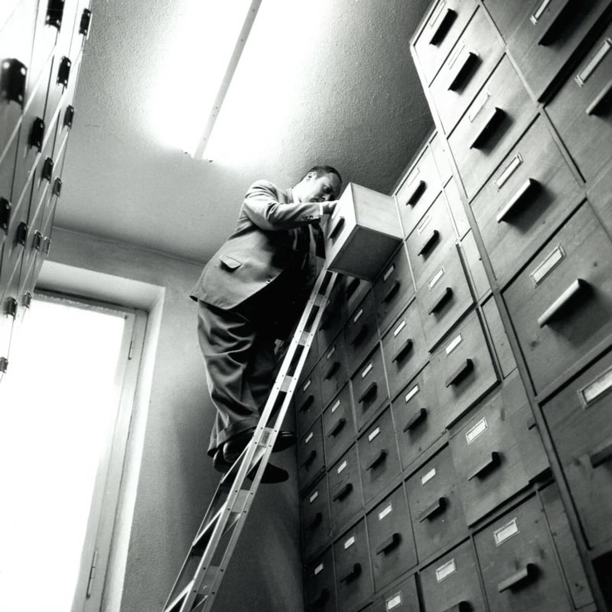 Ein Mann steht auf einer Leiter und macht eine Archivschublade auf. 