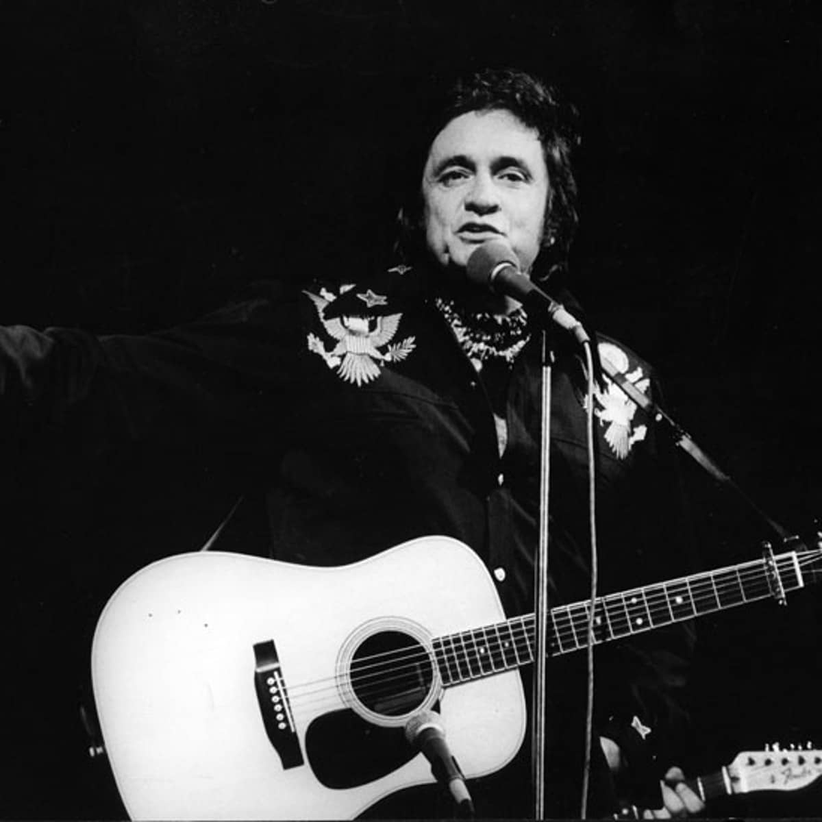 Johnny Cash mit einer Gitarre und Mikrophon auf der Bühne