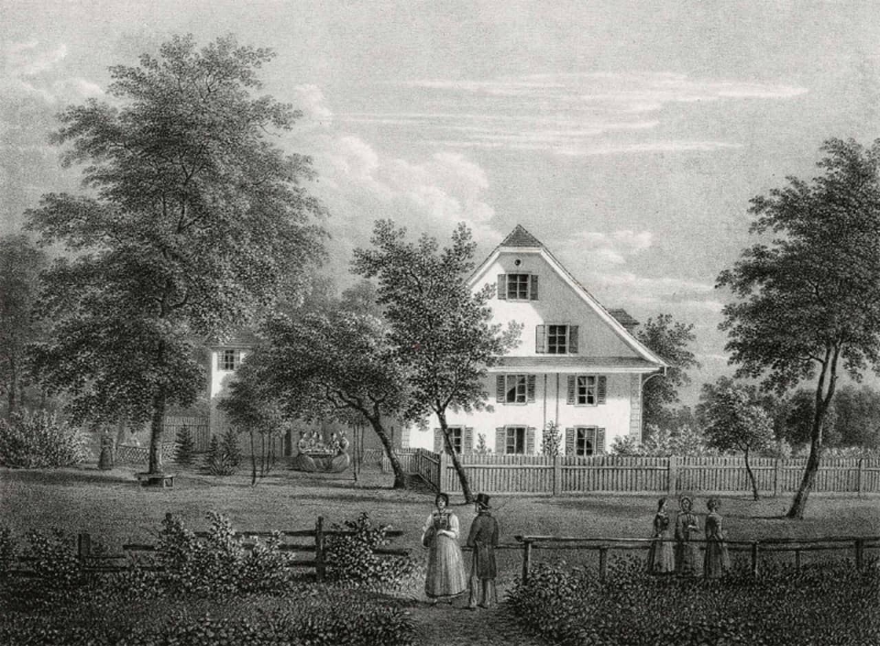 Schwarz-weiss Zeichnung auf Papier. Ein Haus mit Garten und Parkanlage zu sehen. Bäume stehen im Park. Im Vordergrund sind mehrere Personen zu sehen. In der Nähe des Hauses steht ein Tisch an dem Frauen sitzen. 