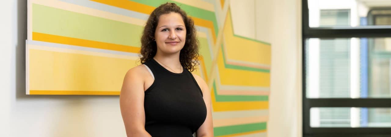 Mächen steht vor gelb, grün, orangem Bild