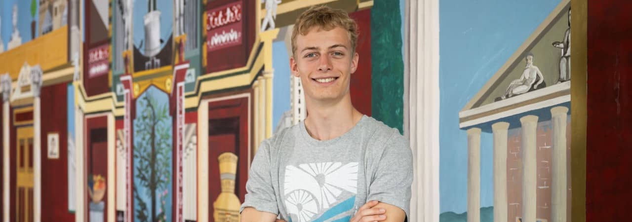 Junge steht vor Wandbild mit ägptischer Vase.