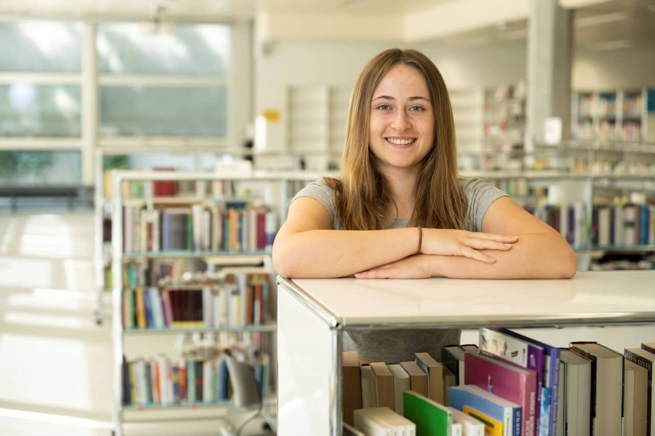 Mädchen stützt sich auf weisses USM-Gestell mit Büchern ab.