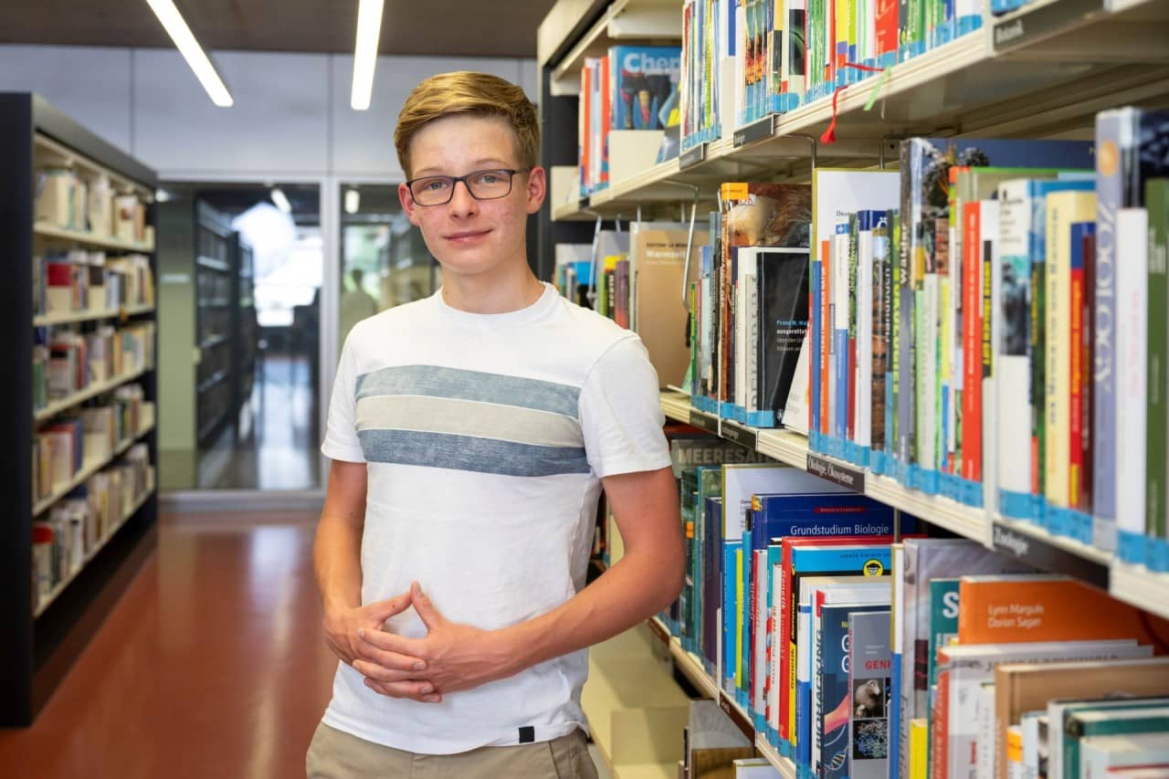 Junge mit Brille sthet vor Büchergestell