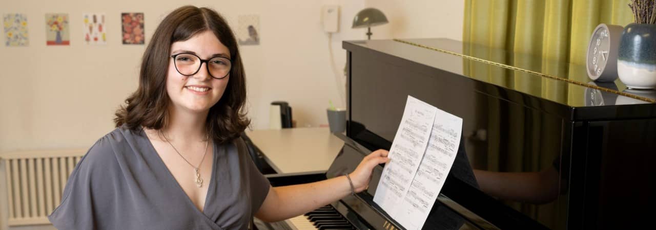 Mädchen mit Brille sitzt vor Klavier und hält Notenblatt