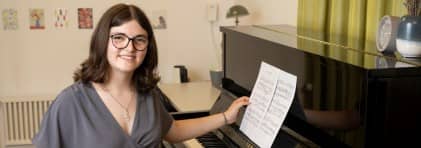 Mädchen mit Brille sitzt vor Klavier und hält Notenblatt