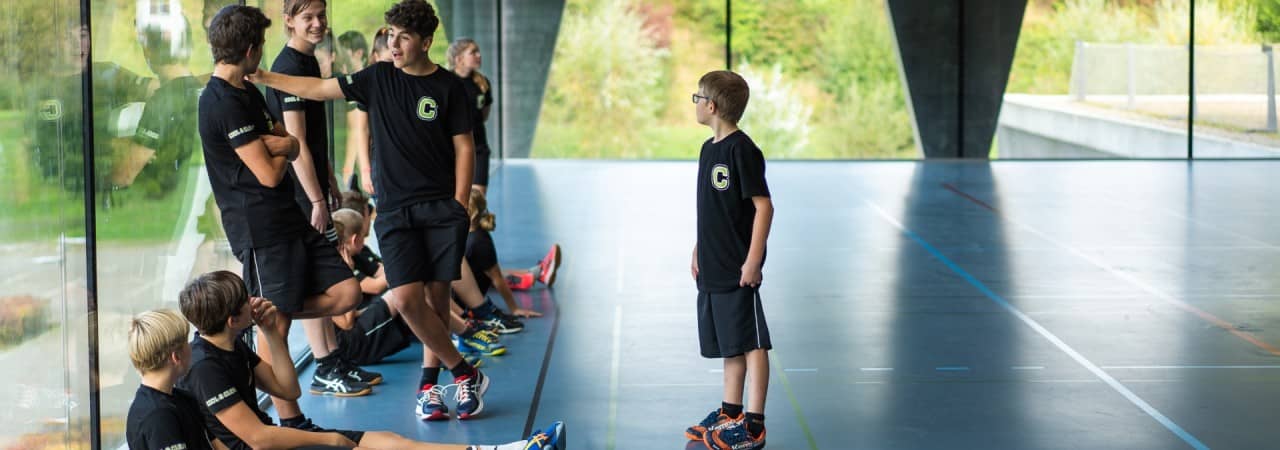 Jugendlche stehen und sitzen in der Turnhalle und diskutiern miteinander.