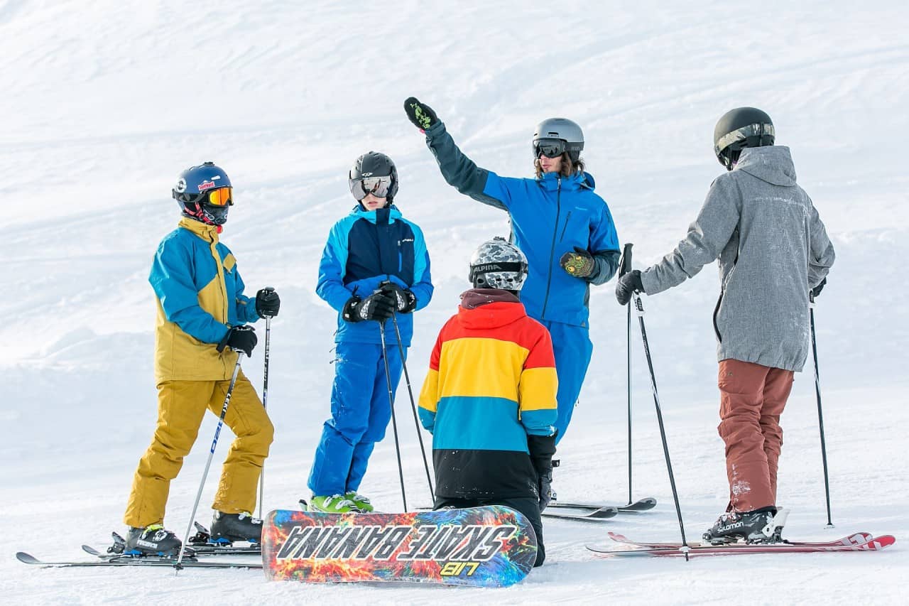 Skifahrer und Snowboarder warten auf der Piste und hören dem J+S-Leiter zu.