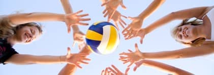 Sechs Mädchen strecken ihre Arme zu einem Kreis. In der Mitte ist ein Volleyball.