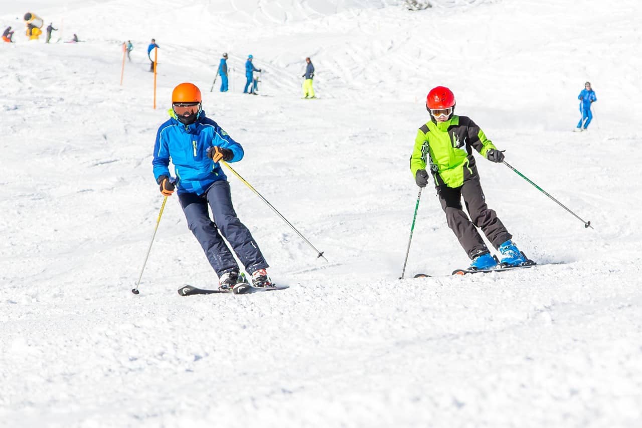 Zwei Skifahrer/innen fahren die Piste hinunter.