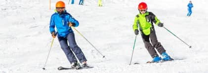 Zwei Skifahrer/innen fahren die Piste hinunter.