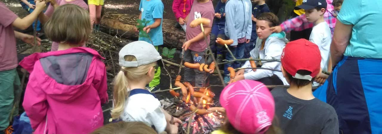 Kinder braten eine Wurst über dem Feuer