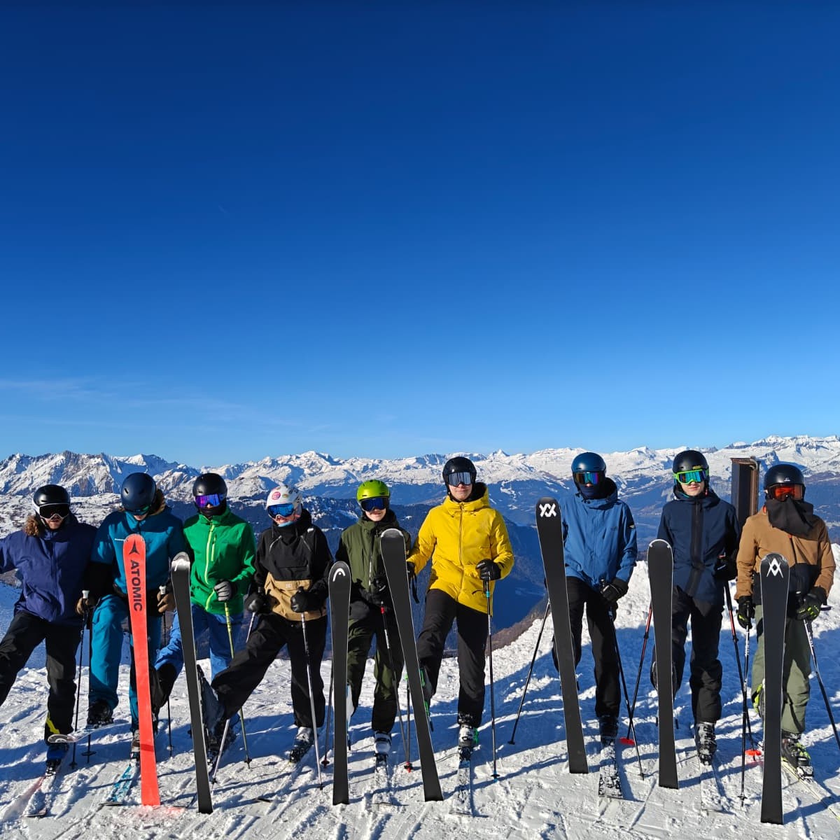Neun Personen posieren mit ihren Skis im Schnee.