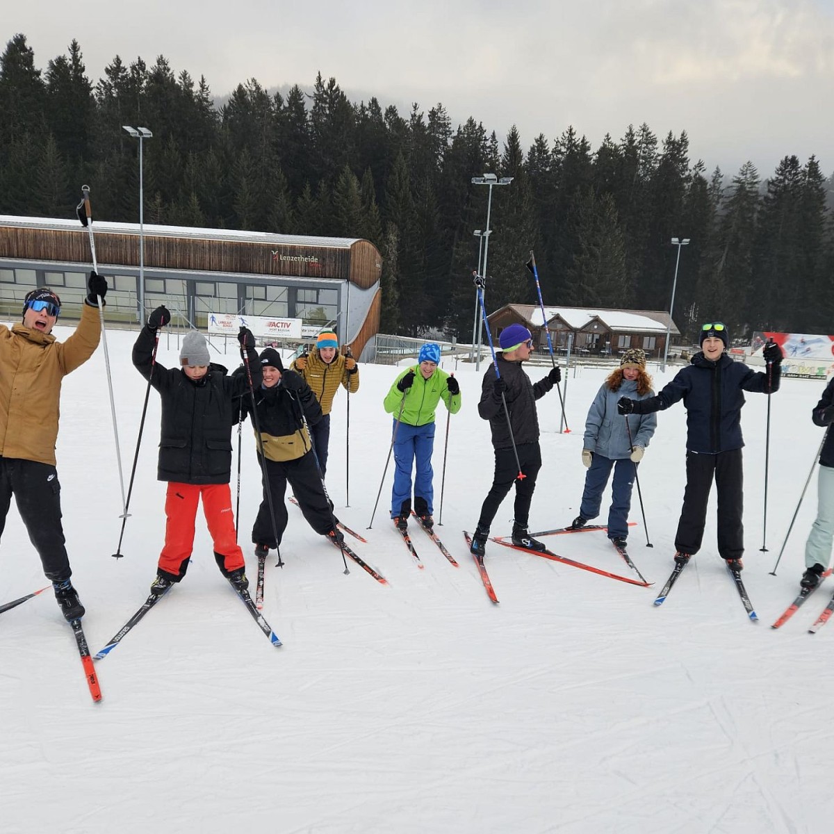 Neun Personen posieren mit den Langlaufskis im Schnee.