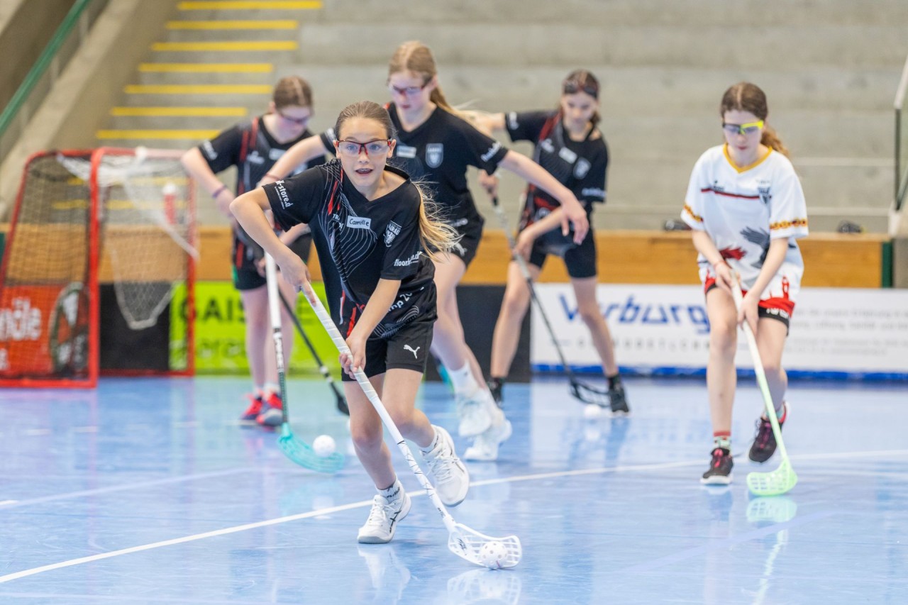 Mehrere Mädchen spielen in der Halle Unihockey.