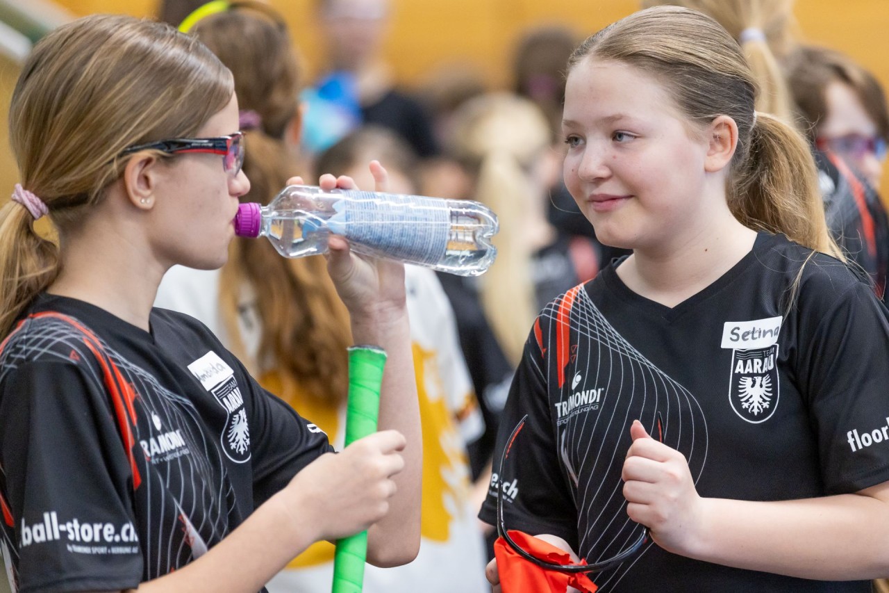 Zwei Mädchen die Unihockey spielen, unterhalten sich auf dem Spielfeld in der Sporthalle.