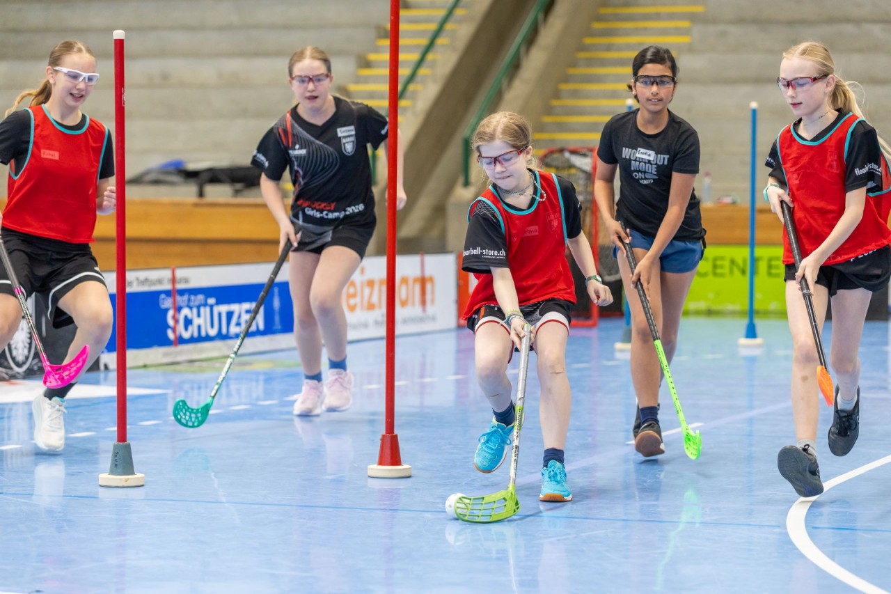 Mehrere Mädchen spielen in der Halle Unihockey.