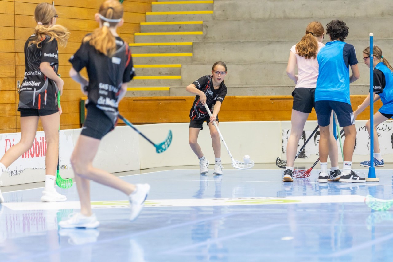 Mehrere Mädchen spielen in der Halle Unihockey.