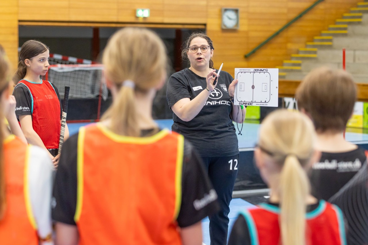 Die Trainerin zeigt den Unihockeyspielerinnen den Spielablauf.