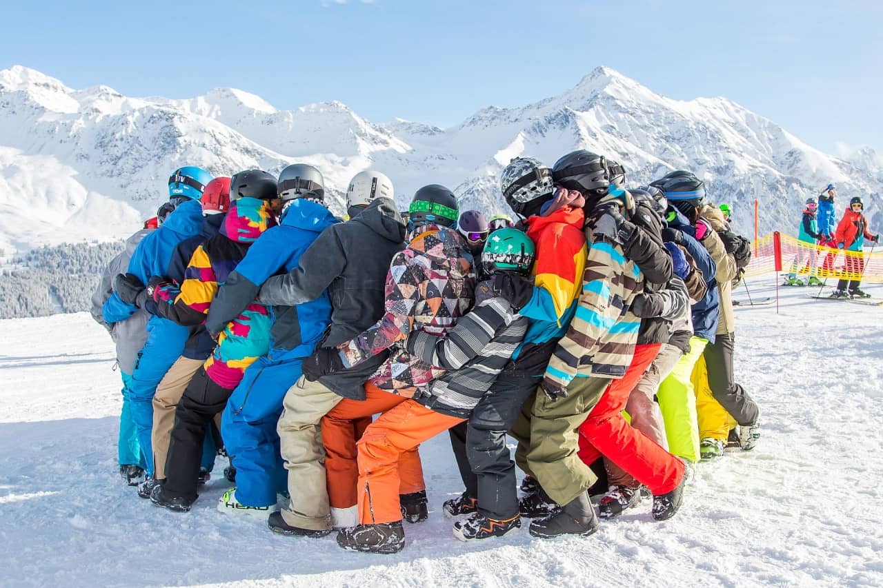 Jugendliche in Ski-/Snowboardbekleidung bilden einen Kreis auf der Piste.