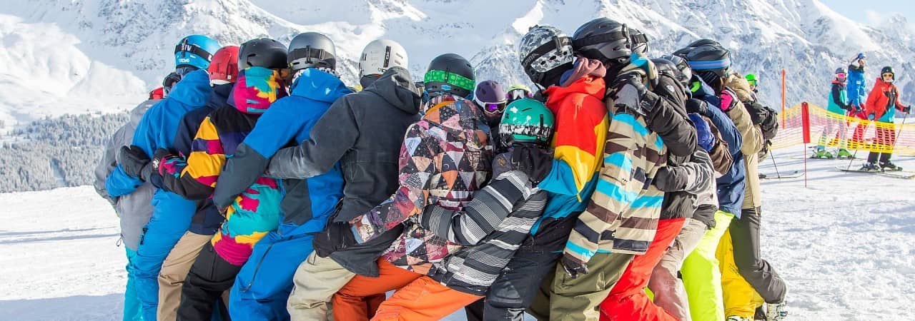 Jugendliche in Ski-/Snowboardbekleidung bilden einen Kreis auf der Piste.