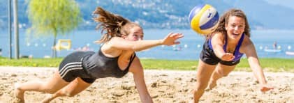 Zwei Jugendliche spiele Beachvolleyball und hechten nach dem Ball.