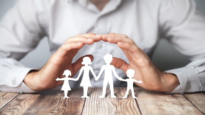Mann hält hütend Hände über vierköpfige Familie aus Papier