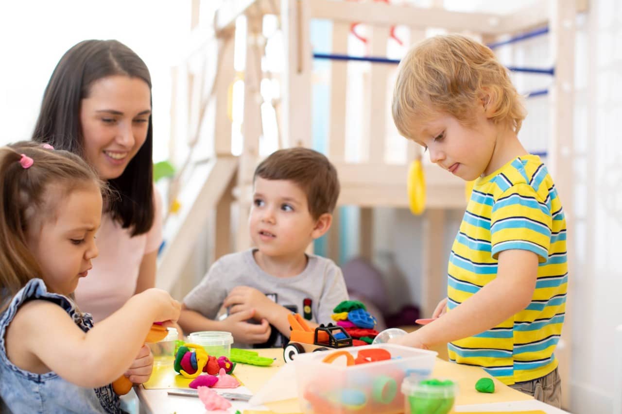 Frau sitzt mit drei spielenden Kindern am Tisch.