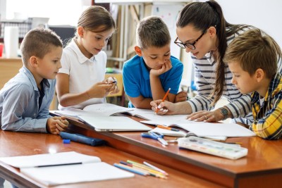 Lehrerin korrigiert umring von Kinder in einem Schreibheft.