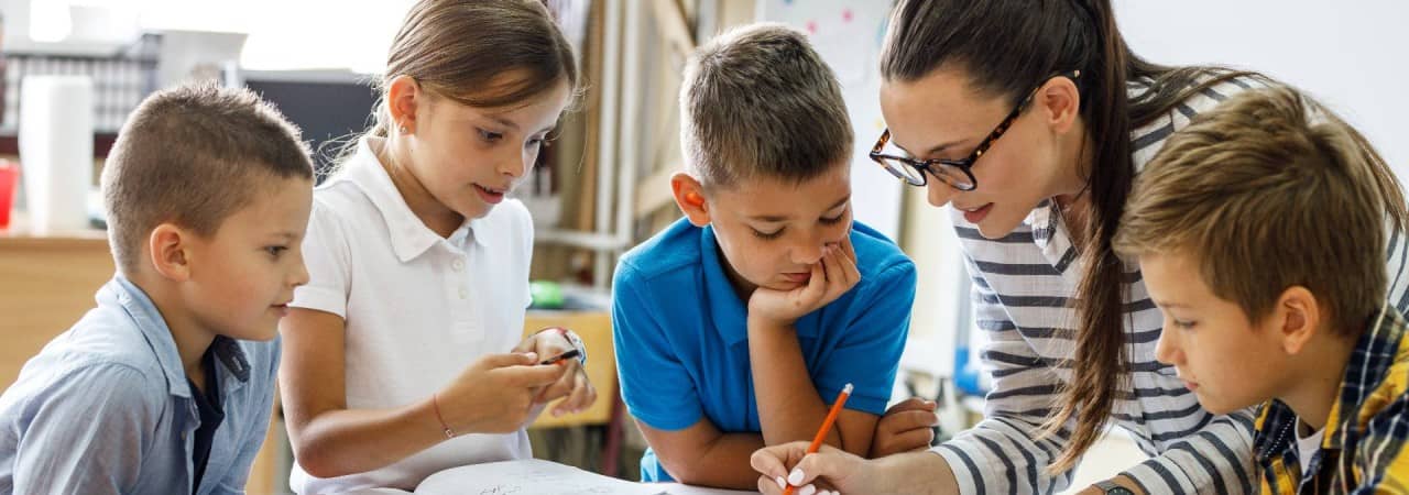 Lehrerin korrigiert umring von Kinder in einem Schreibheft.