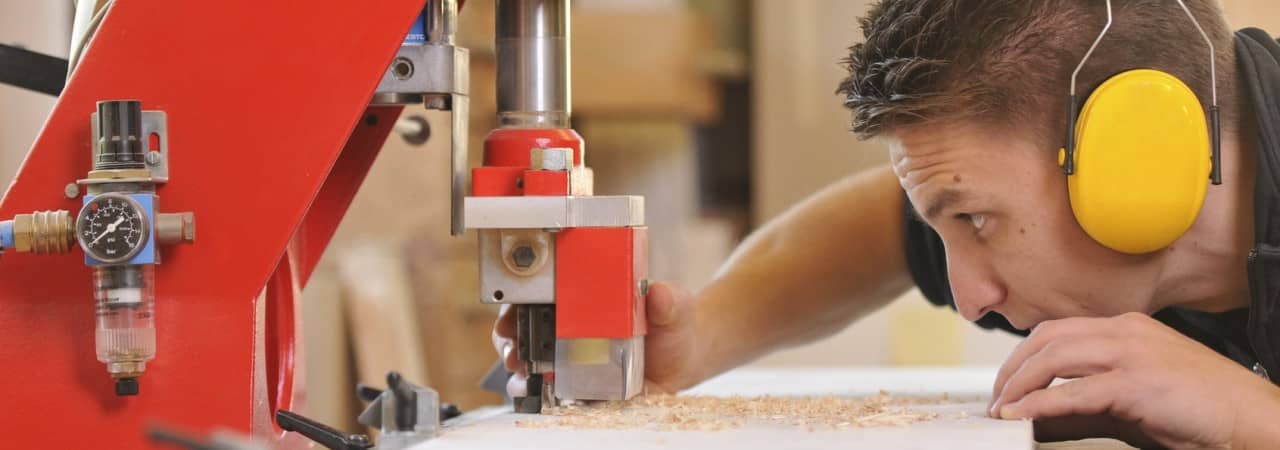 Ein junger Schreiner schneidet mit einer Sägemaschine ein Holzbrett zurecht.