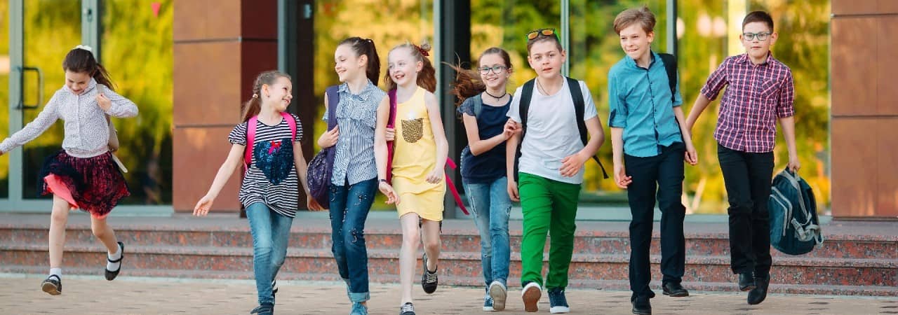 Acht Schülerinnen und Schüler vor einem Schulgebäude laufen in Richtung der fotografierenden Person.