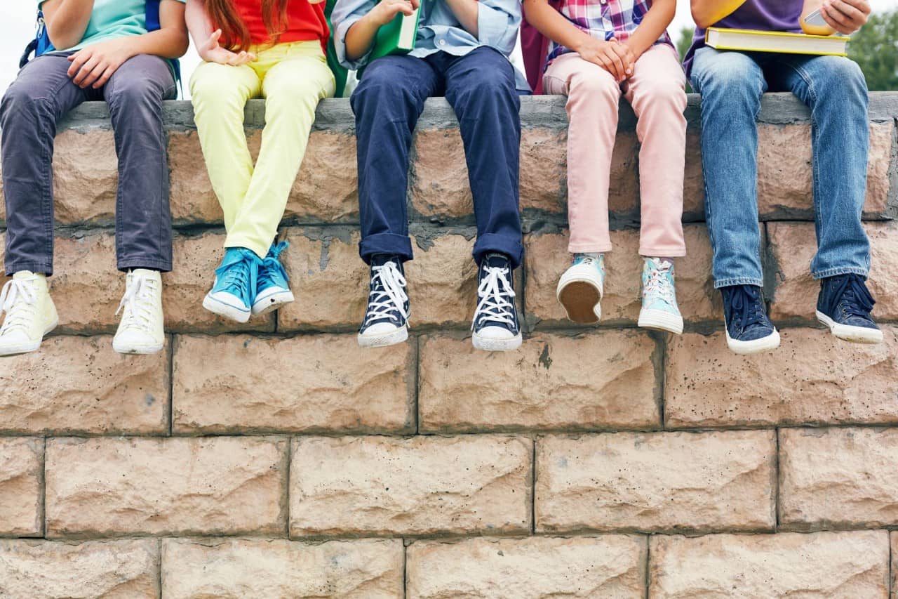 Fünf Schulkinder sitzen auf einer Mauer. Man sieht nur ihre Beine.