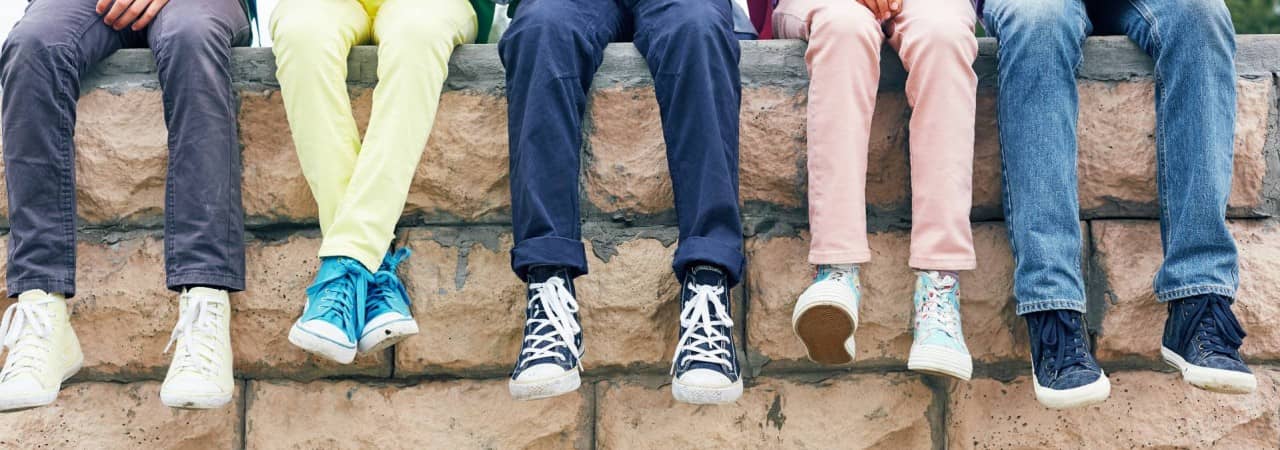 Fünf Schulkinder sitzen auf einer Mauer. Man sieht nur ihre Beine.