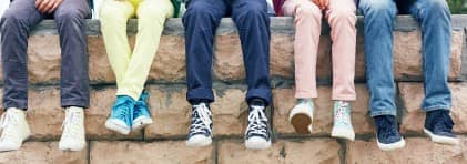 Fünf Schulkinder sitzen auf einer Mauer. Man sieht nur ihre Beine.