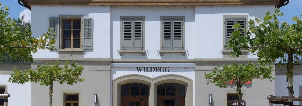 Bahnhofsgebäude vom Bahnhof Möriken-Wildegg, davor sind 4 Bäume zu sehen. 