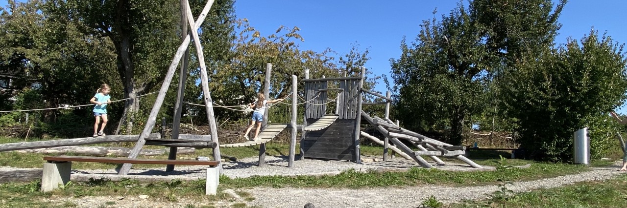 Das Bild zeigt einen naturnahen Spielplatz mit natürlichen und sickerfähigen Materialien als Fallschutz.
