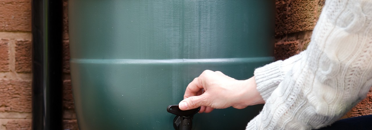 Eine Giesskanne wird mit Wasser aus einer Regenwasserfassung befüllt.