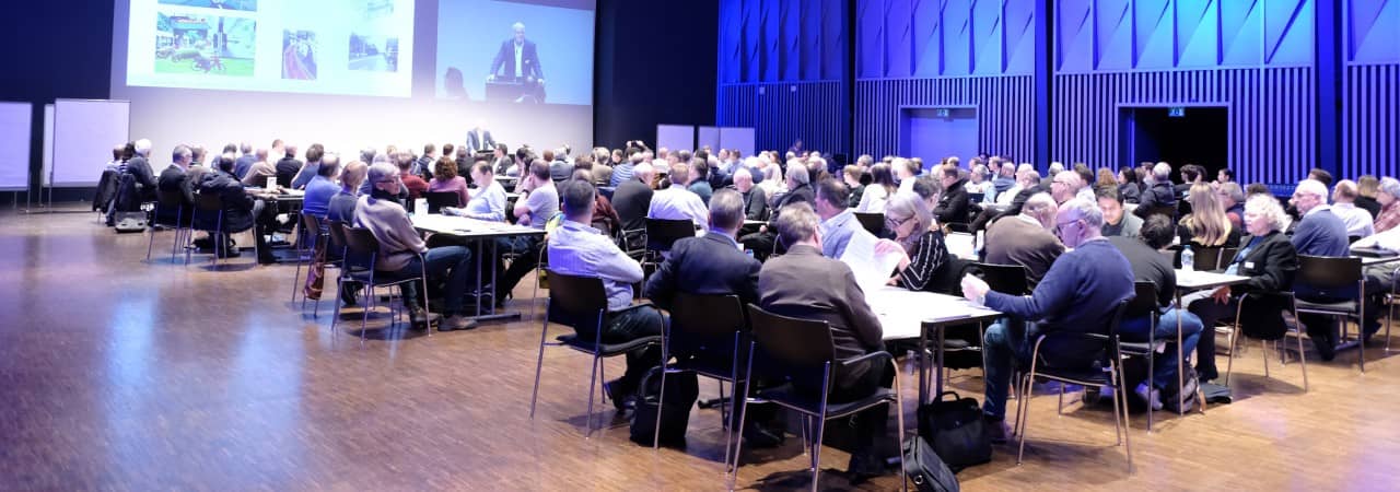 Blick in eine Saal, in dem die Teilnehmenden an Tischen gemeinsam diskutieren.