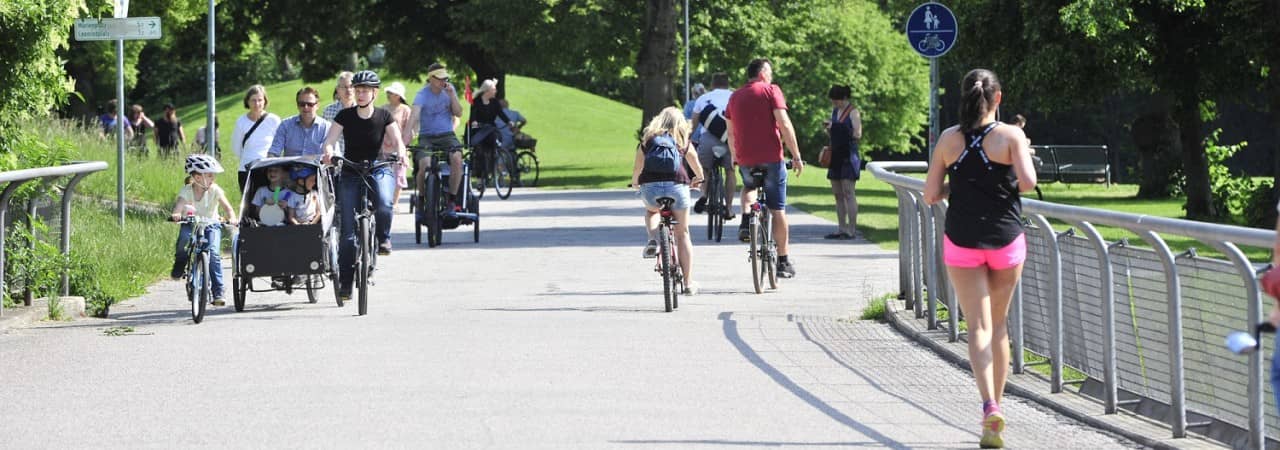 Menschen gehen zu Fuss oder mit dem Fahrrad über einen Weg in einer Grünfläche