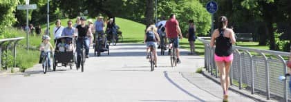 Menschen gehen zu Fuss oder mit dem Fahrrad über einen Weg in einer Grünfläche