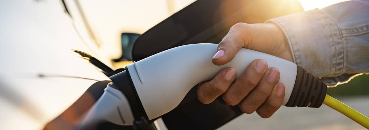 Eine Hand steckt einen Ladestecker in ein Elektroauto