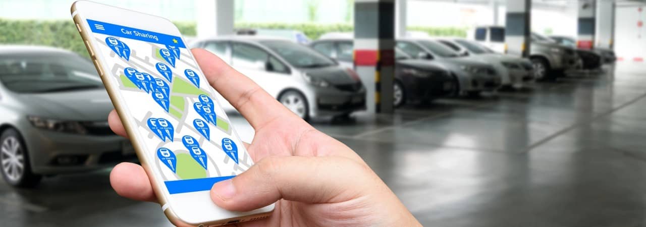 Carsharing App auf einem Mobiltelefon mit Autos im Hintergrund