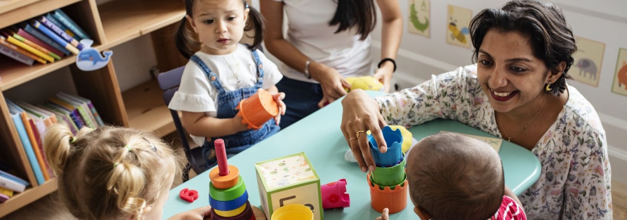 Betreuungsperson spielt mit Kindern am Tisch.