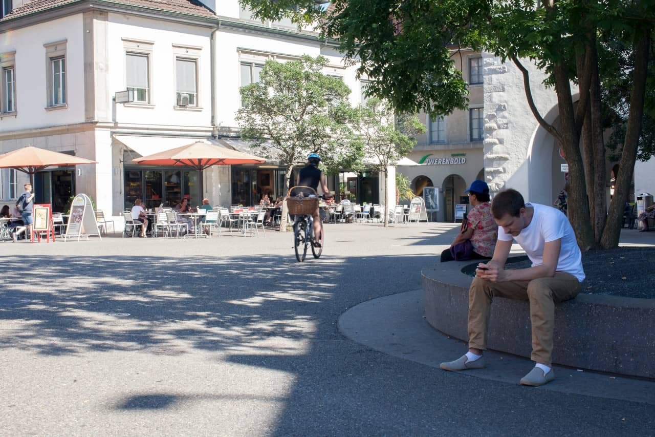 Menschen sitzen auf dem Schlossbergplatz im Schatten eines Baumes.