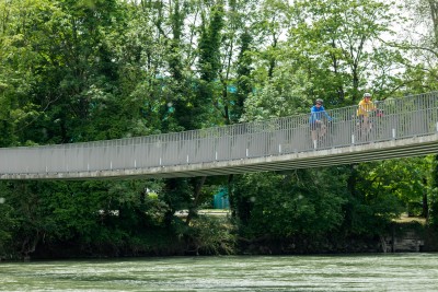 Sicht vom Flussufer auf zwei Velofahrende auf dem Aaresteg in Windisch.