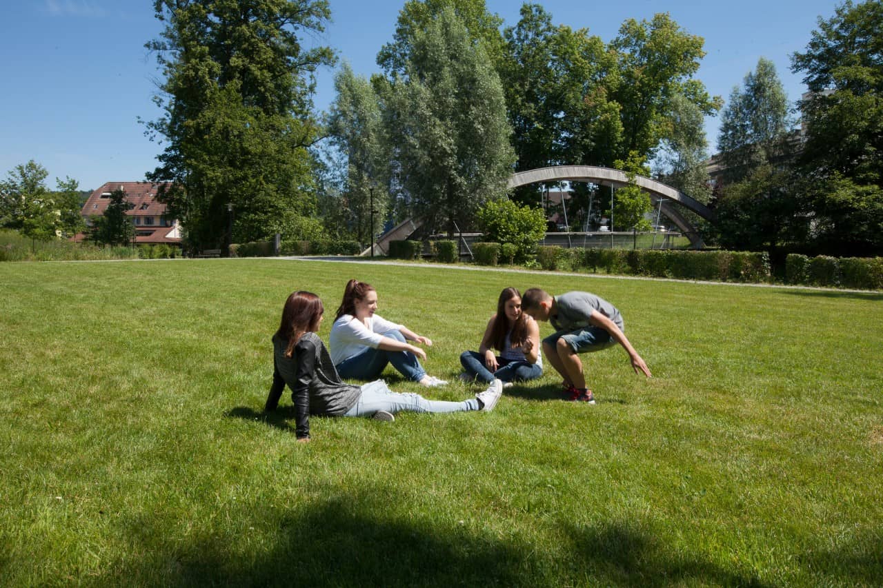 Jugendliche sitzen auf einer Rasenfläche.