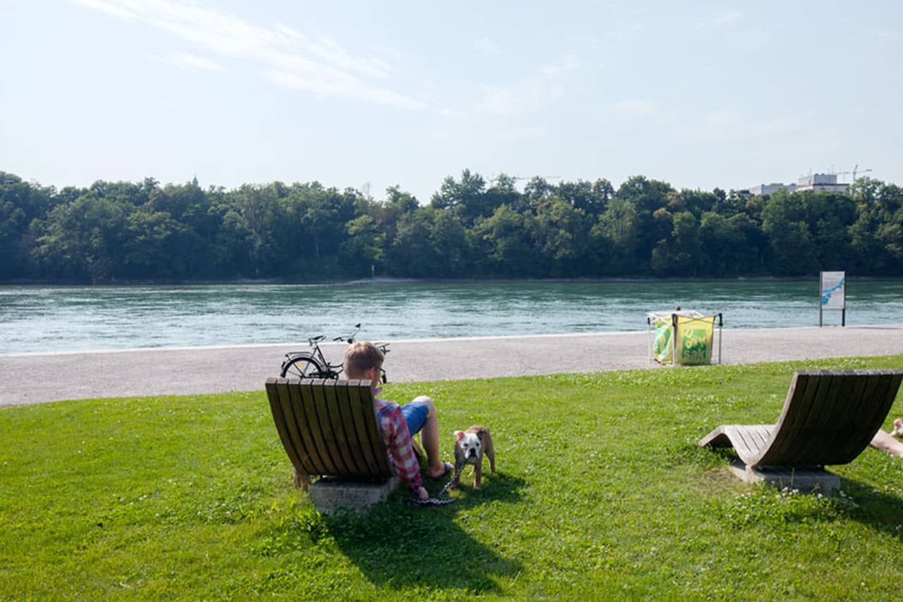 Ein Mann mit Hund sitze auf einer Holzliege mit Blick Richtung Fluss