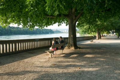 Zwei Frauen sitzen auf einer Holzbank an der Rheinpromenade im Stadtpark in Rheinfelden.
