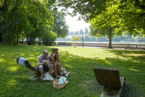 Ein Mann und eine Frau teilen sich eine Holzliege und picknicken im Park